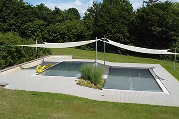 Rechteckiger Pool mit Abdeckung, umgeben von Rasen und Bäumen, mit Sonnensegeln und gelbem Schwimmtier.