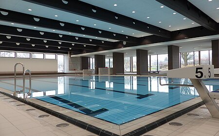 Das Monheimer Hallenbad, das Jurabad, mit gefülltem Schwimmbecken, Startblöcken und großen Fenstern, die Tageslicht hereinlassen.