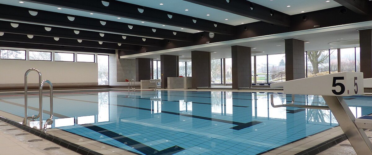 Das Monheimer Hallenbad, das Jurabad, mit gefülltem Schwimmbecken, Startblöcken und großen Fenstern, die Tageslicht hereinlassen.