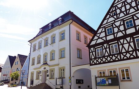 Straßenansicht der Monheimer Innenstadt: Im Vordergrund das Rathaus der Stadt Monheim, mit weiteren mehreren Gebäuden, darunter ein Fachwerkhaus, das man Schindlerhaus nennt.