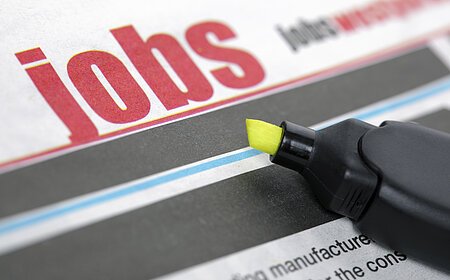 Zeitungsseite mit dem Wort "Jobs" in großen roten Buchstaben und ein gelber Textmarker liegt auf der Zeitung.